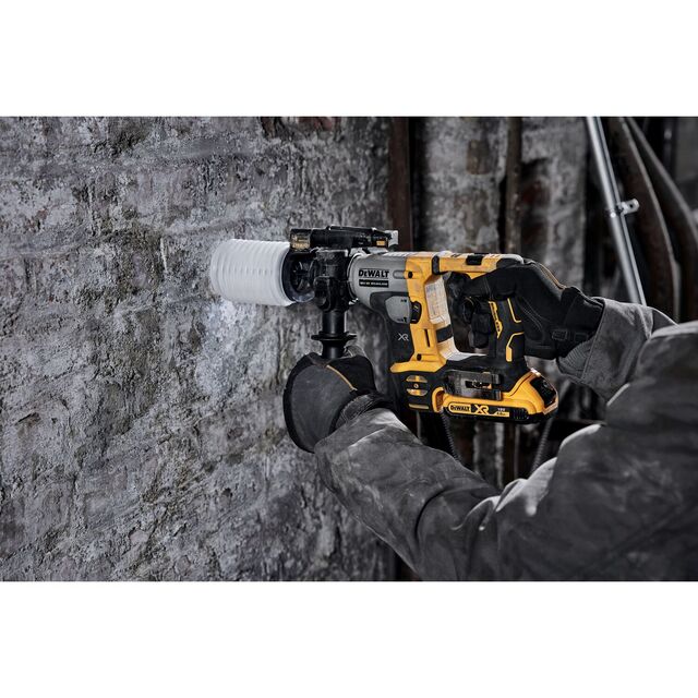 Person i arbetskläder borrar i en rå stenmur med en gulsvart Dewalt borrmaskin.