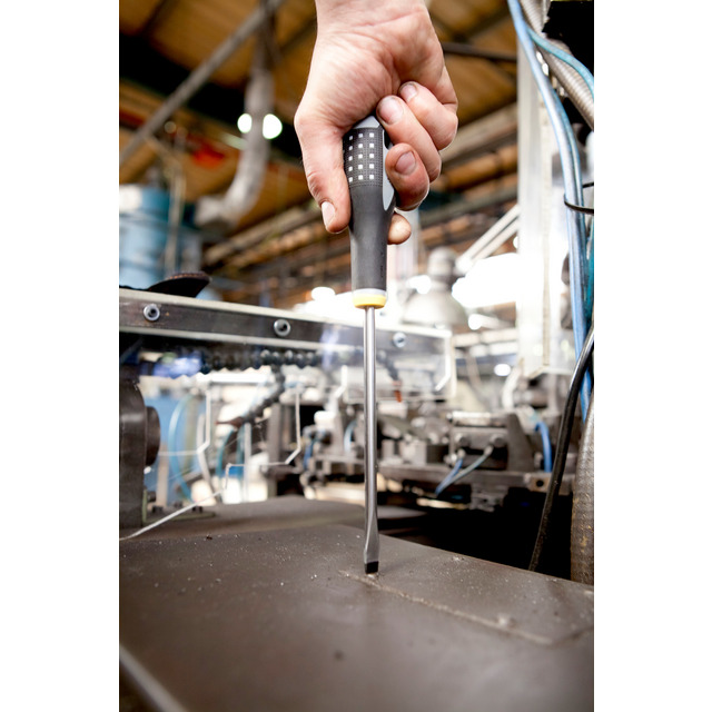 Hand som håller en skruvmejsel ovanför en industrimaskin i en fabriksanläggning.