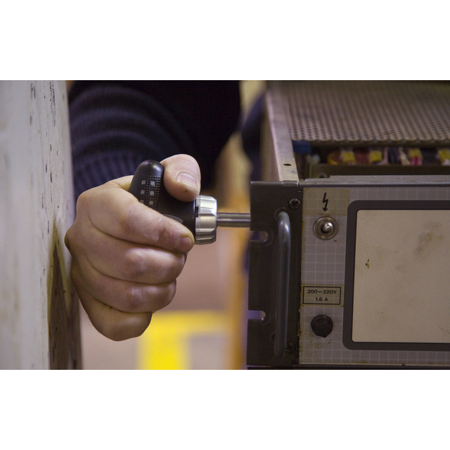 Hand som justerar en ratt på en elektrisk apparat med etiketterna 200-220V och 16A.