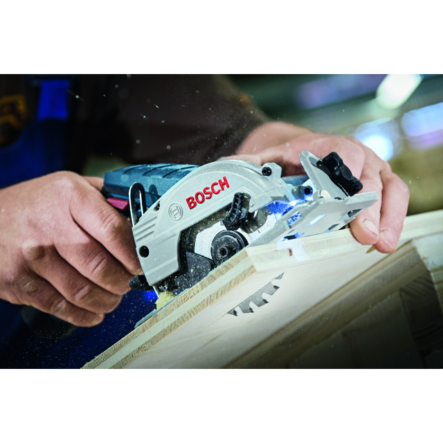 En hand håller en Bosch mini-cirkelsåg som sågar i en träplanka.