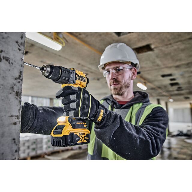 En person i hjälm och reflexväst använder en gul och svart borrmaskin för att borra i en betongpelare.