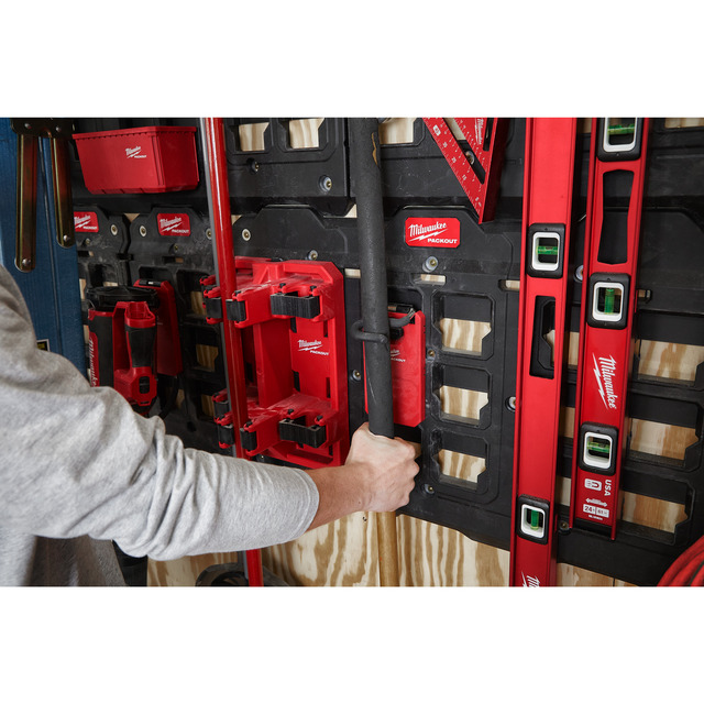 En person använder ett väggmonterat Milwaukee Tool hållarsystem för att förvara verktyg och utrustning.