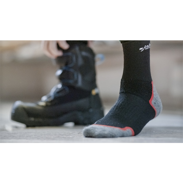 Svart och grå strumpa med röd häl vid sidan av en svart stövel på ett grått golv.