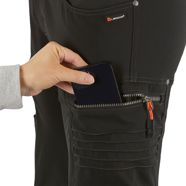 Hand som stoppar en svart smartphone i en svart byxficka med röd dragkedja.