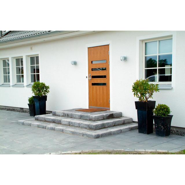 Trappa av grå stenplattor leder upp till en orange dörr med glasrutor, omgiven av vita väggar och fönster. Två växter i krukor.