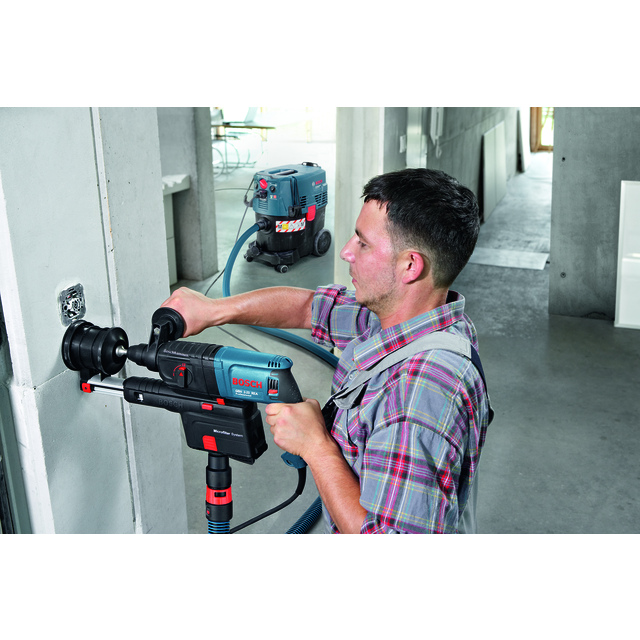 Man using a power drill to make a hole in a wall, with a vacuum system attached for dust collection.