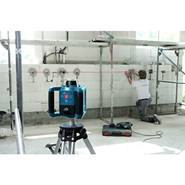 Laserinstrument på stativ används i byggarbetsplats, arbetare justerar installationer på väggen.