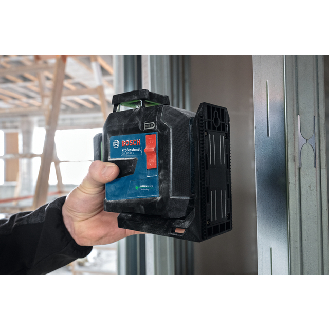 En person håller en Bosch Professional lasermätare framför en stålregel i en byggnad under konstruktion.