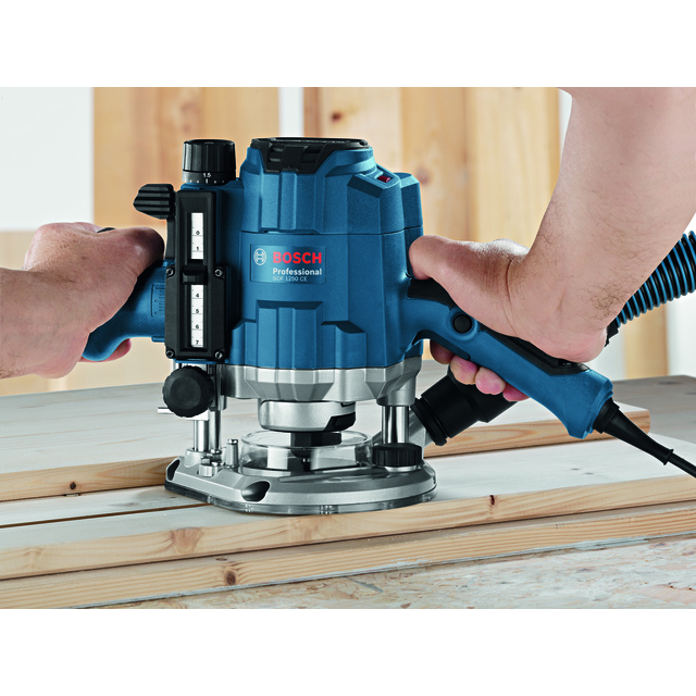 En blå och svart Bosch router används för att fräsa trä på en arbetsyta.