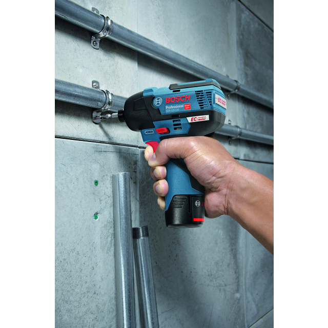 En hand håller en Bosch Professional borrliknande verktyg och arbetar med metallrör på en betongvägg.