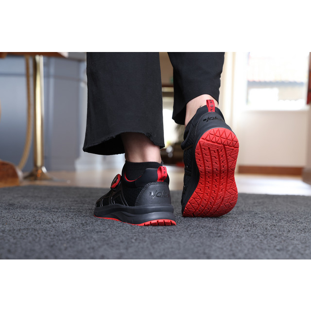 En person går på en matta med svarta sneakers som har röda sulor och detaljer.