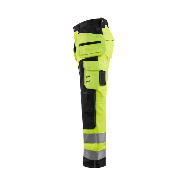 Arbetsbyxa i gul och svart med reflexband och flera fickor, sedd från sidan.