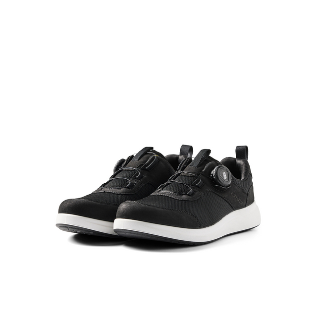 Svarta sneakers med vita sulor, snörning och en dekorativ metallbit med bokstaven B.