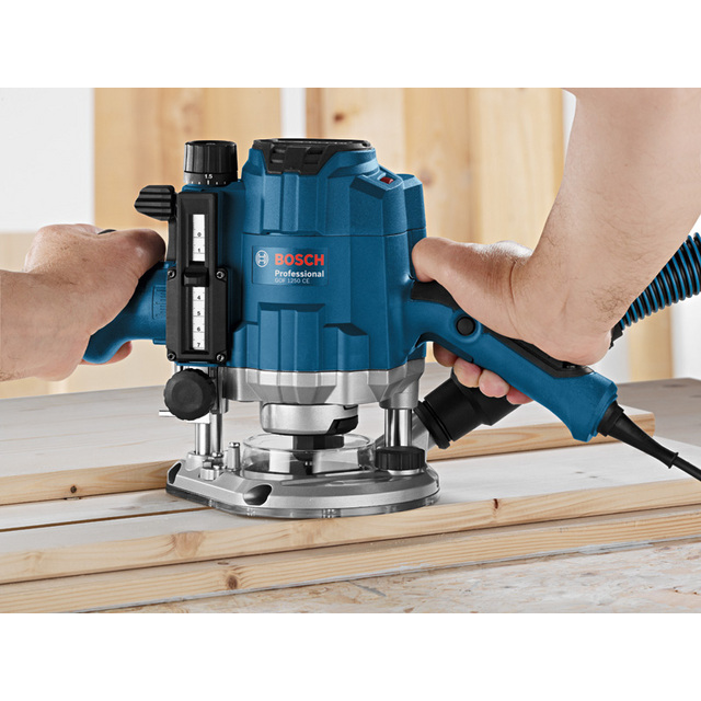 Två händer använder en blå Bosch Professional fräs på träplankor.