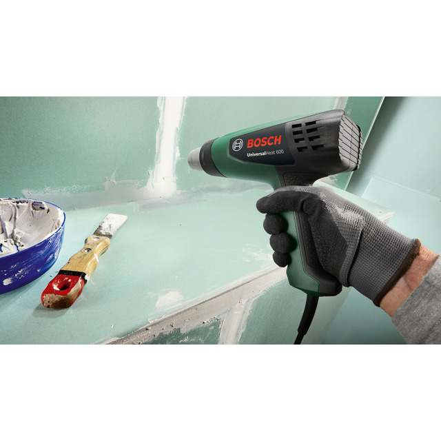 Varmluftspistol från Bosch används vid väggarbete; pensel och blå skål med färgrester intill.