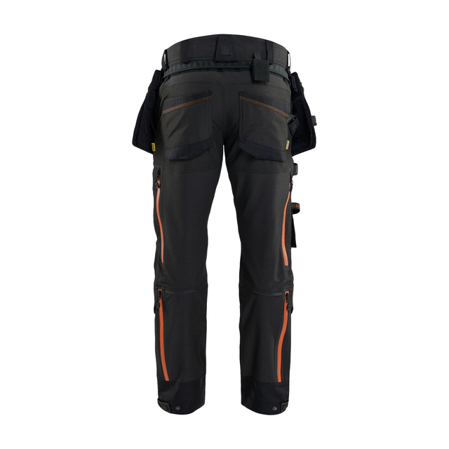 Arbetsbyxor i mörkt material med orange detaljer, flera fickor och verktygshällor på sidorna.