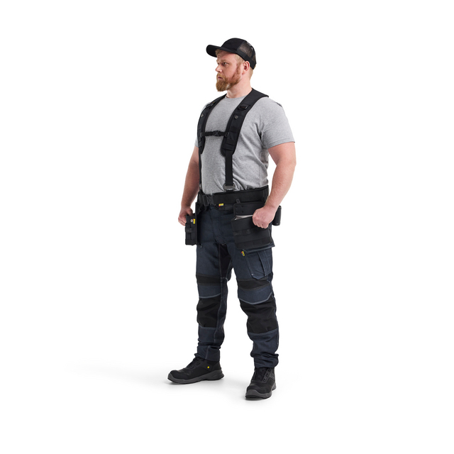Person wearing a grey t-shirt, black cap, utility belt and dark pants with knee pads in a standing pose.