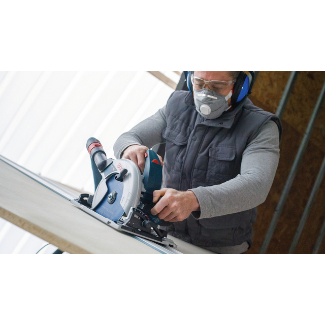 Person with goggles and mask using a circular saw on a wooden board.