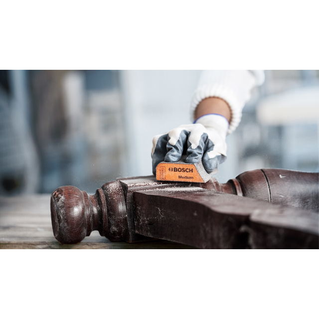 En person slipar en träyta med ett Bosch-sandpapper.