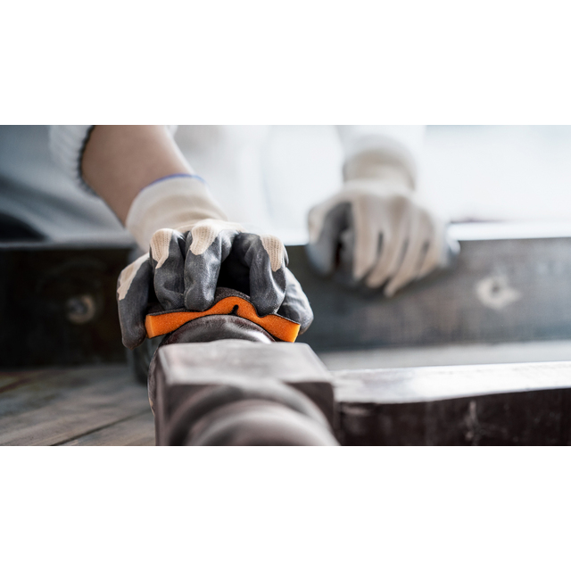 Händer i arbetshandskar som håller i metallverktyg på träyta.