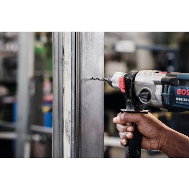 En person använder en Bosch borrmaskin för att borra i en metallram, med suddig bakgrund.