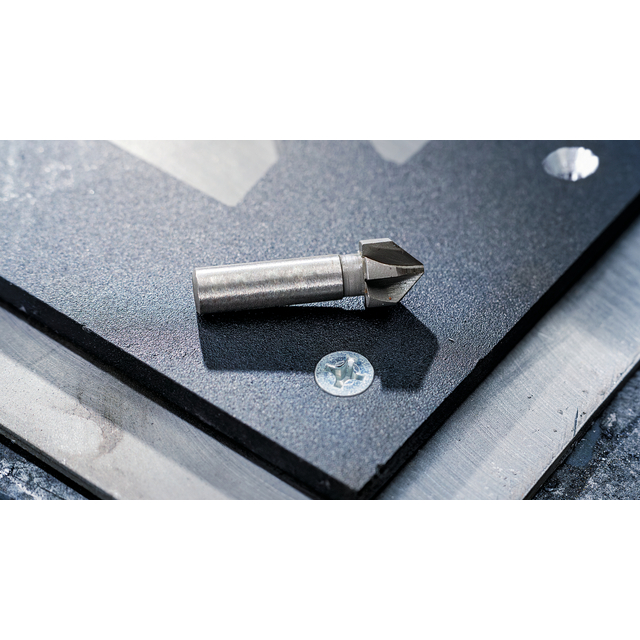 Metallkon eller borrhuvud placerad på en svart skiva av glas eller sten, med fästelement bredvid.