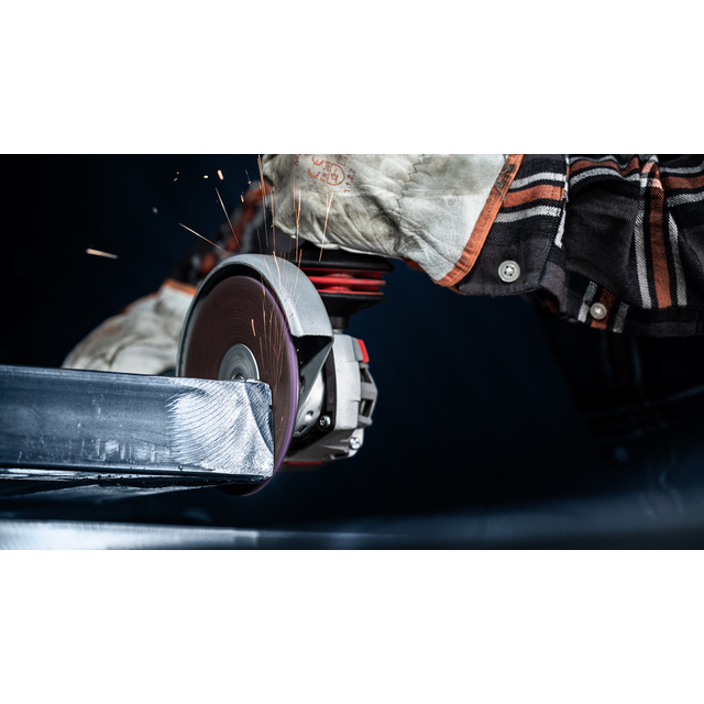 En person slipar metall med vinkelslip, gnistor flyger. Personen bär skyddshandskar och skogsrutig skjorta.