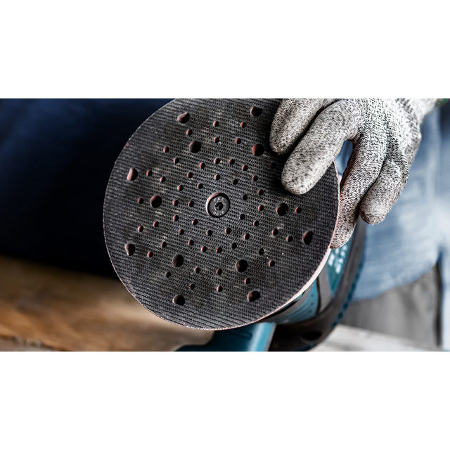Rund slipmaskin med perforerad slipplatta, hålls av handskbeklädd hand.
