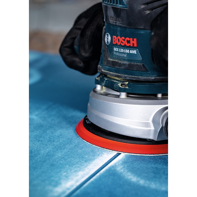 Två händer håller en Bosch GEX 125-150 AVE Professional excenterslip på en blå yta.