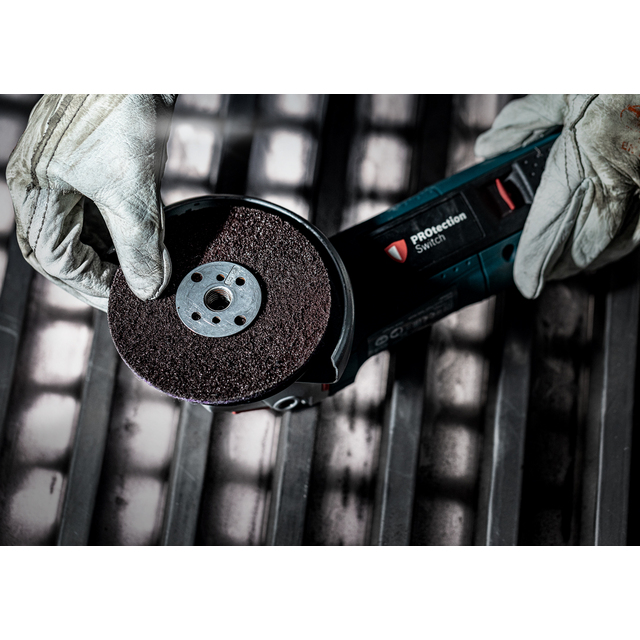 En person med handskar håller i en vinkelslipmaskin med en brun sliprondell över ett metallgaller.