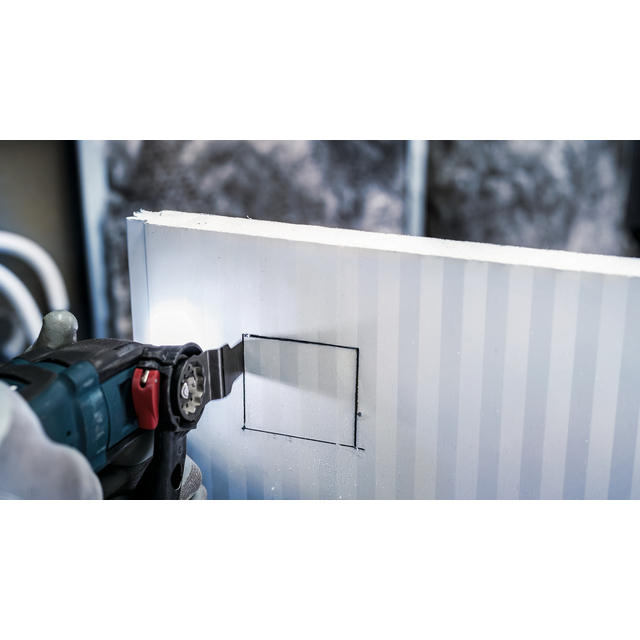 En person skär en rektangel i en styv isoleringsskiva med en elektrisk såg.