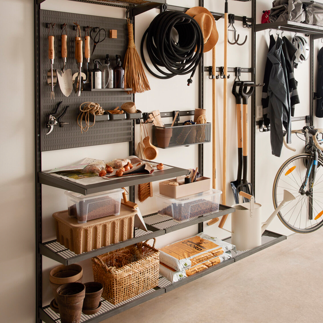 Hylla i garage med trädgårdsverktyg, korgar och plastlådor. Hängande hattar och redskap på krokar. cykel i bakgrunden.