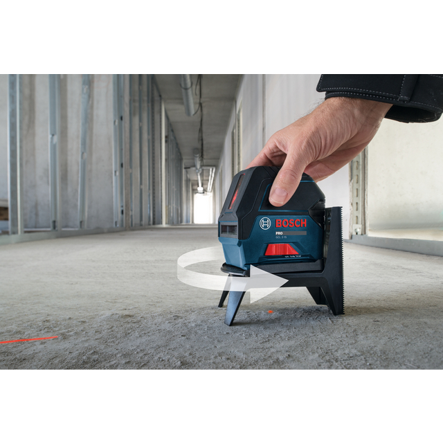 Man håller en Bosch lasermätare som projicerar en röd linje på ett betonggolv i ett rum under konstruktion.